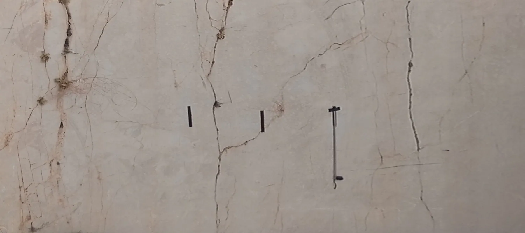 Rectified photo of a marble quarry face with black tape marks and a hanging measuring tape. Amber marks show where each visible discontinuity crosses the horizontal reading line.